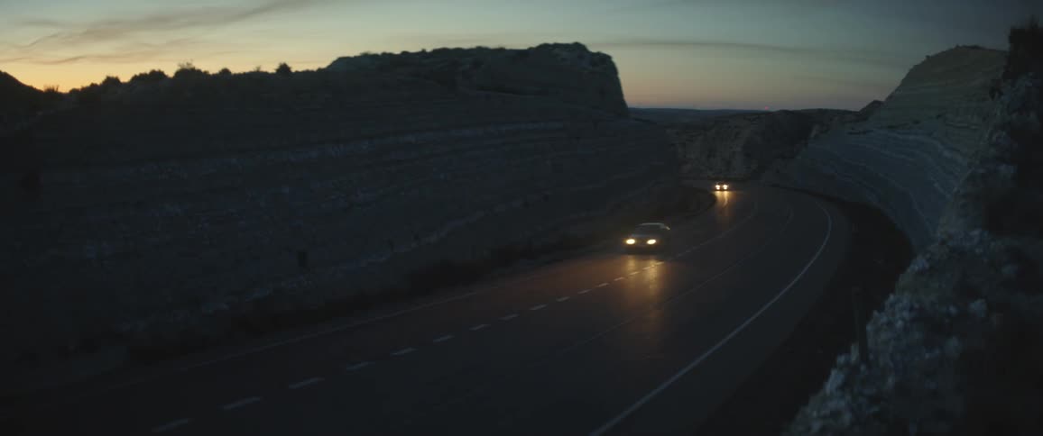 Cars driving with headlights on a road through a mountain pass at sunset