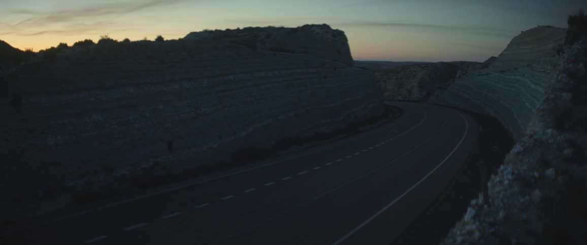 A shipping truck and a car drive on a quiet road at dusk