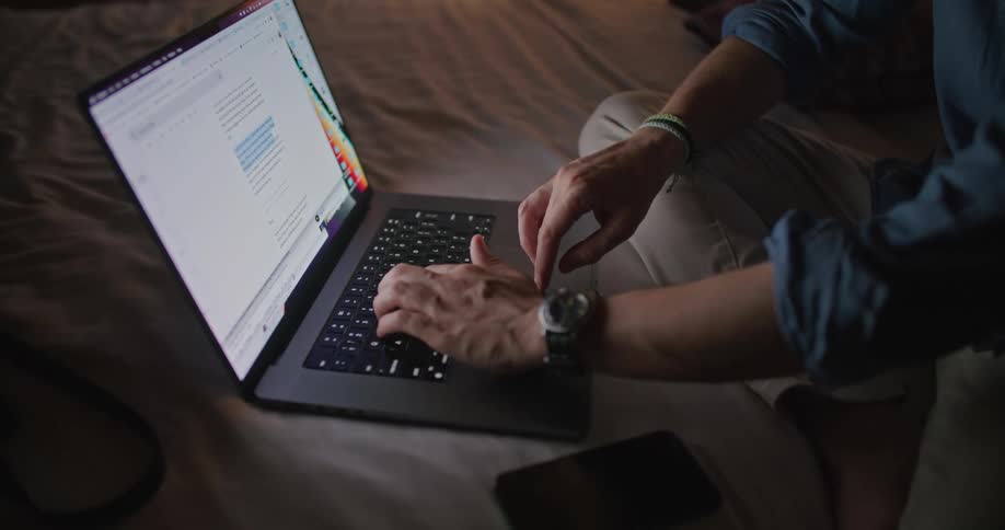 A man is sitting indoors and typing on a laptop