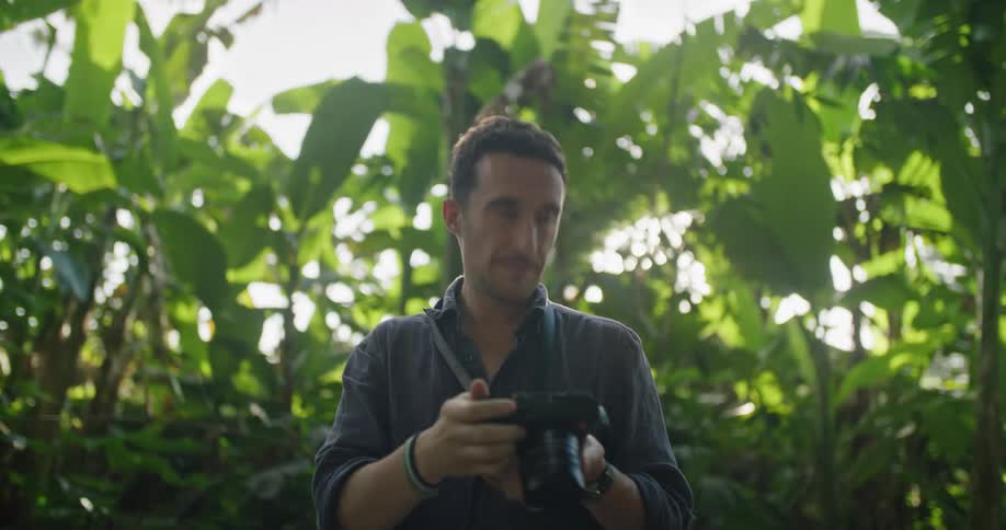 A man is standing in a rainforest looking around and taking pictures