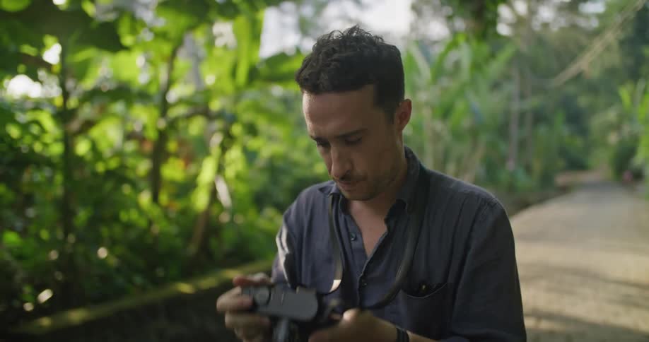A man taking a photograph with a camera and then smiling in a jungle climate