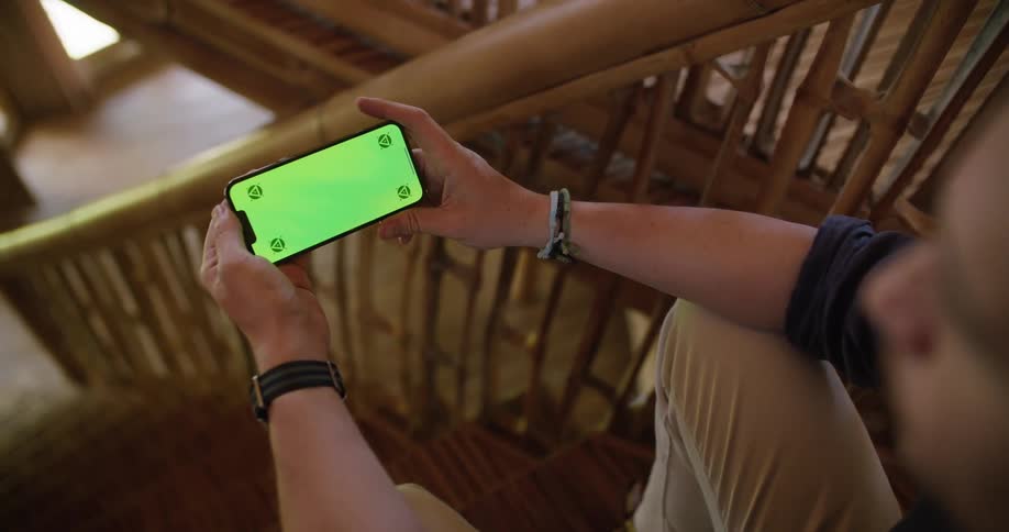 A man is sitting on stairs holding a cell phone with a green screen