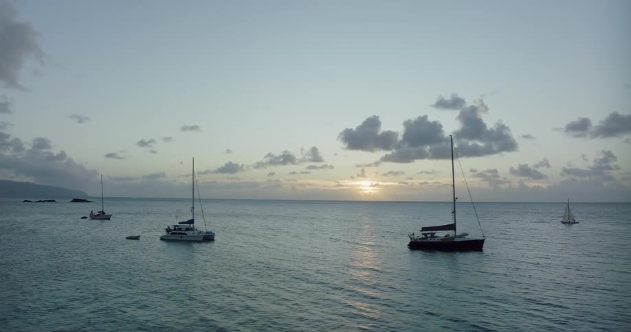 Sun sits on the horizon shining across boats anchored a distance from shore