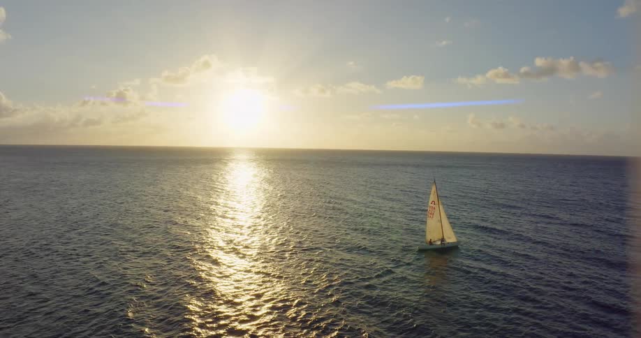 An aerial view of a sailboat floating on ocean water at sunset