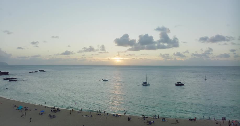 People relaxing on a sandy tropical beach with sailboats on the water