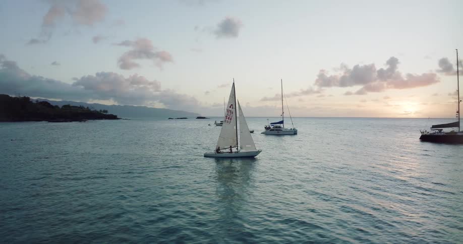 Aerial view of sailboats sailing on ocean water near the coast at sunset
