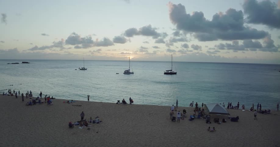 Aerial view of people on the beach and boats sailing on water at sunset