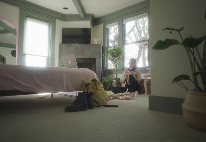 Woman sits on carpeted floor in bedroom sewing