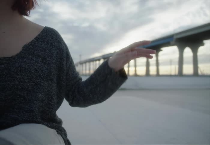 A female sits on a beach and waves her arm around as if to music