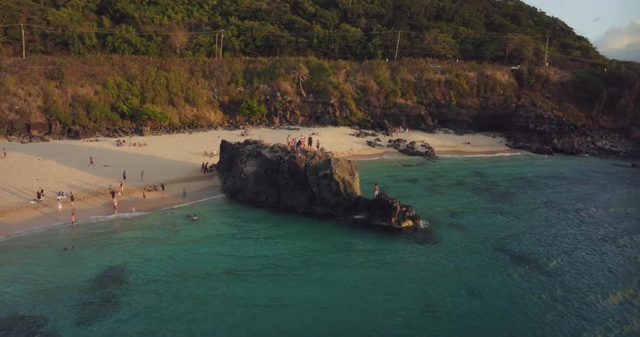 Aerial view of a group of tourists standing on top of a promontory on the beach next to the ocean at evening