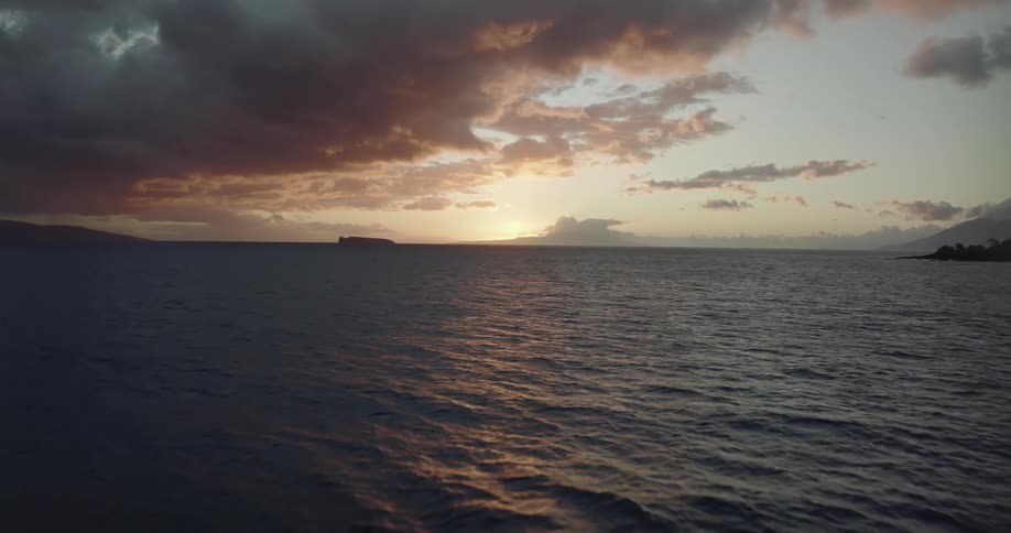 Light reflects on the water as it ripples and waves as darkening clouds hang in the sky and the sun is setting on the horizon