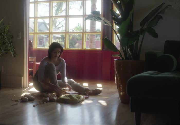 A woman sitting on the hardwood floor putting on her ballet dancing shoes
