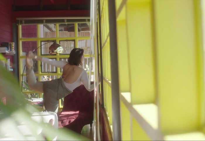 A woman does stretches in front of a window indoors during the day