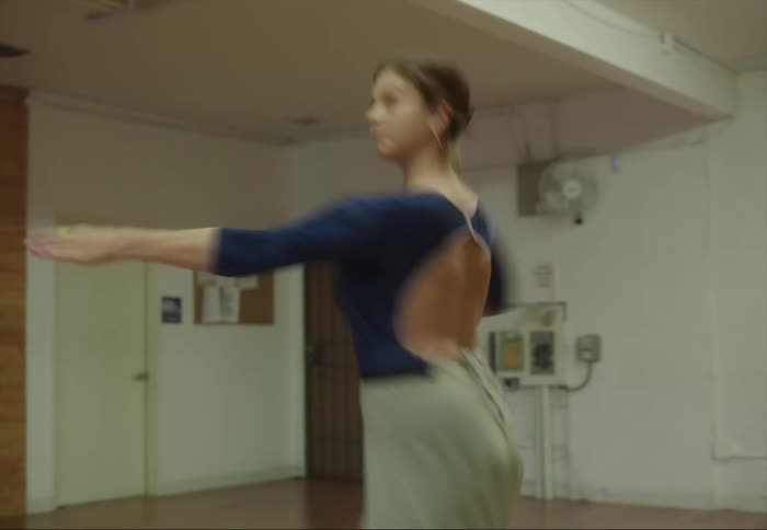 A young woman is practicing ballet dancing in a room and does a pirouette