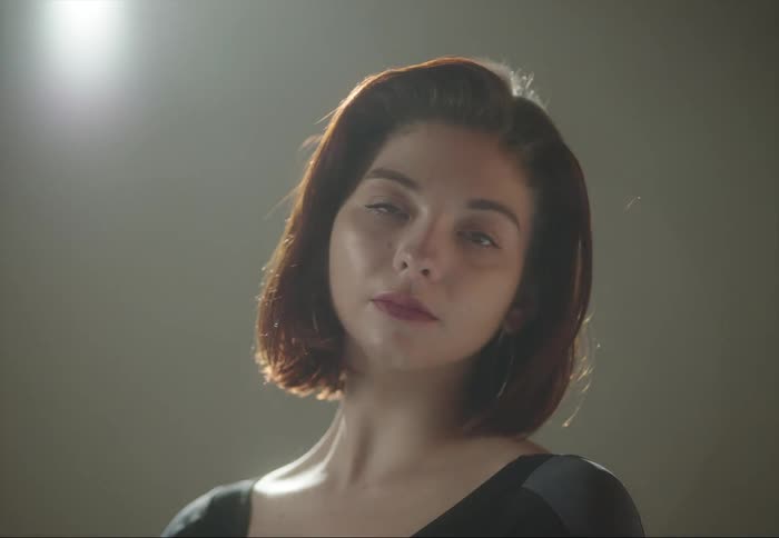 A woman is standing under a light looking ahead as cameras flash