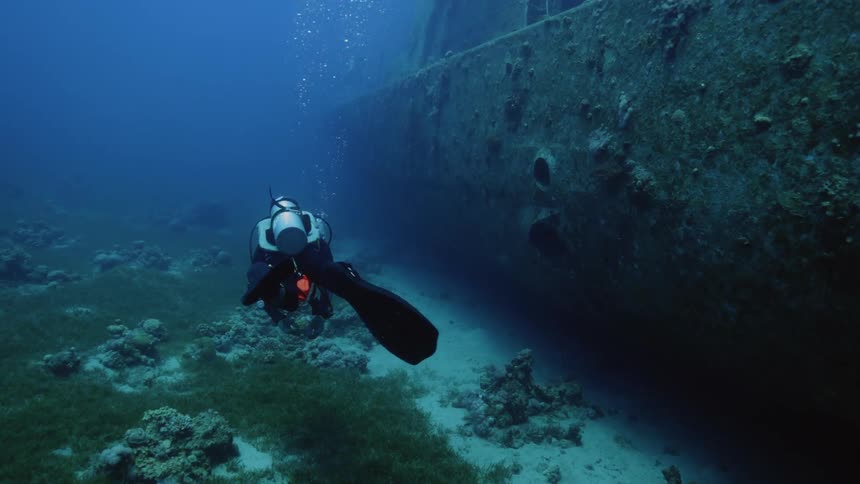 Scuba diver swimming along the wreckage of a sunken ship at the bottom of the ocean