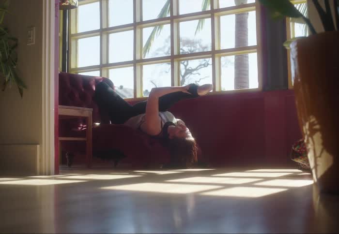 Young woman reclined upside down on a couch in the living room stretching