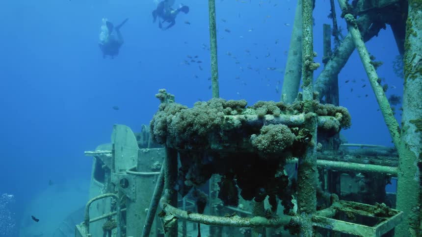 Scuba divers swim through blue water near shipwreck reef