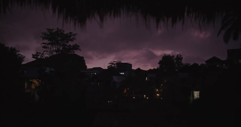 Thatch roofed balcony shows view of town silhouetted under purple cloudy sky