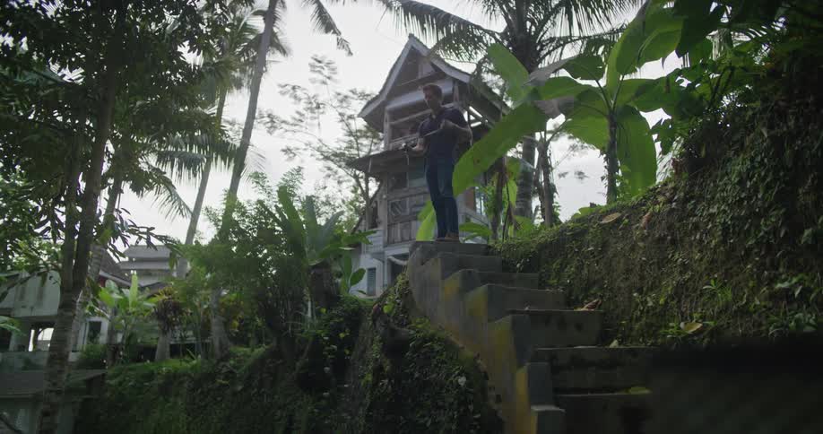 Young man standing at the top of a staircase on a rural area in the tropics takes pictures with a camera