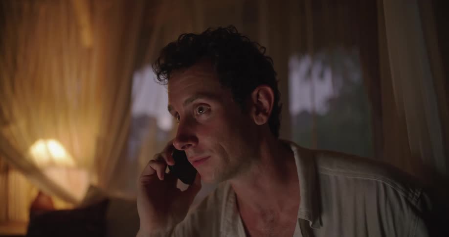 A man is sitting down and smiling as he talks on his phone