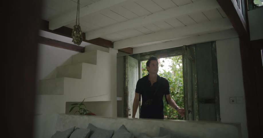 A man opens the double doors to a rural home while wearing a backpack