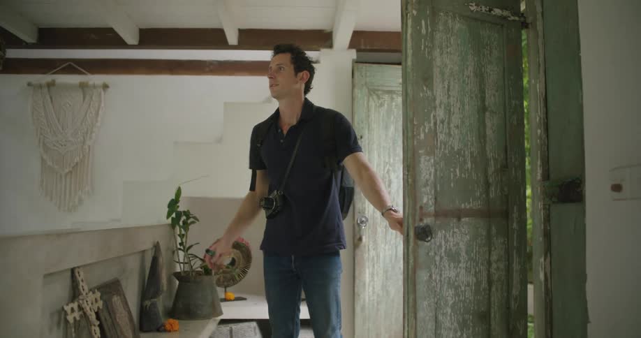 Man with black polo shirt backpack jeans and camera enters building