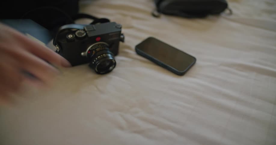 Man picks up a passport and a camera from a bed
