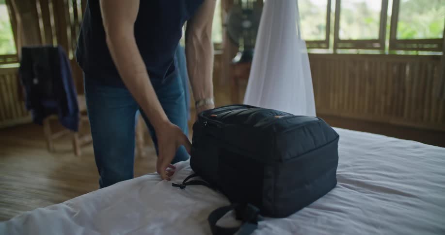 A man is holding his camera and looking at it then he puts it inside a backpack and zips it up and puts it on his back