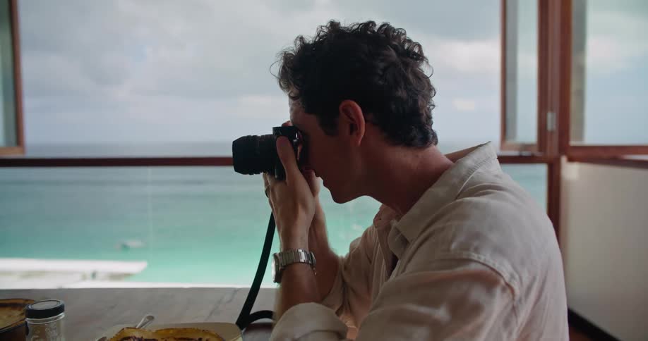 Man takes pictures of a friend eating lunch on an apartment next to the ocean