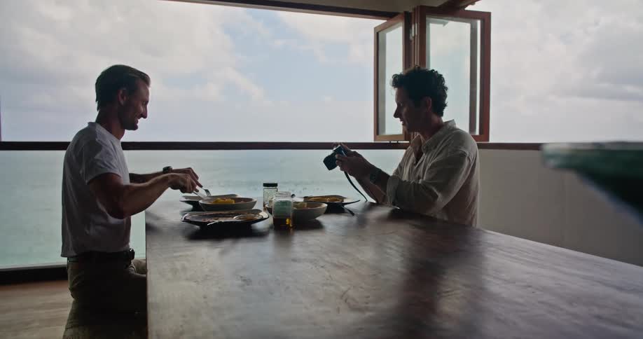 Photographer takes pictures of a man eating on the table on a beachfront apartment