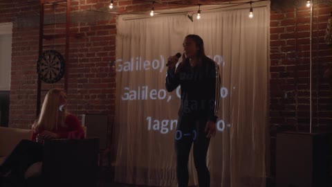 A woman sings karaoke while standing before a curtain with song lyrics projected on the surface