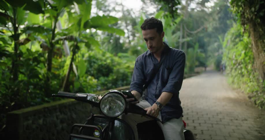 Man sitting on a motorcycle parked on a road on the tropics checking his smartphone