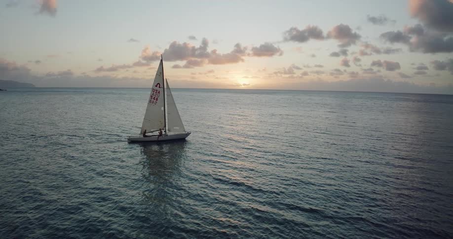 The silhouette of two people sitting on a sailboat sailing away from shore at sunset