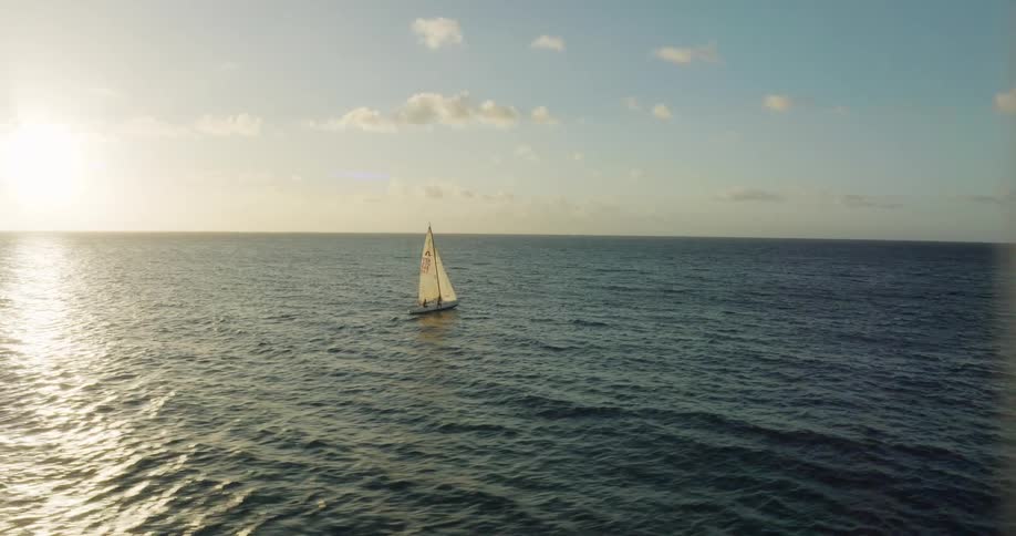 A sailboat sails across the ocean along the coast during the day