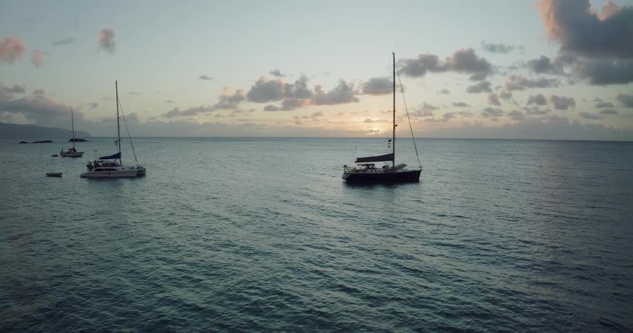 Anchored sailboats with sails down bobbing in the water at sunset