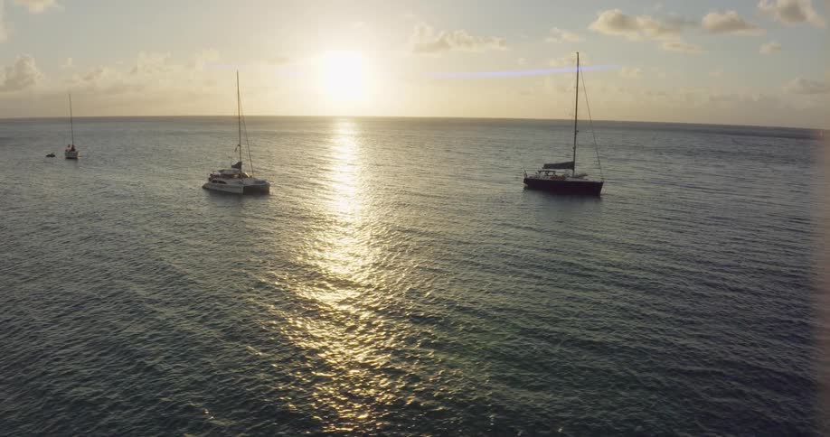 Sailboats anchored near the coast bobbing in the water at sunset