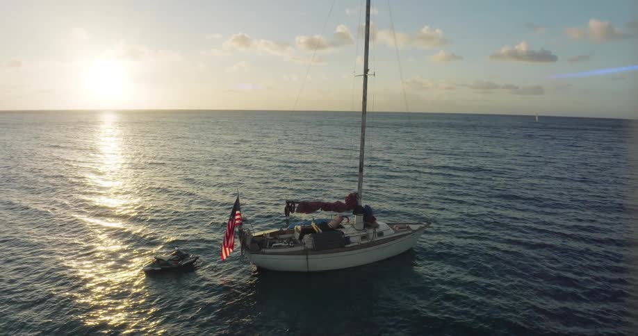 Orbiting aerial view of a sailboat floating on the calm surface of the ocean at evening