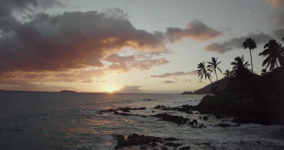 Aerial view of the sun setting over the ocean near a tropical coast