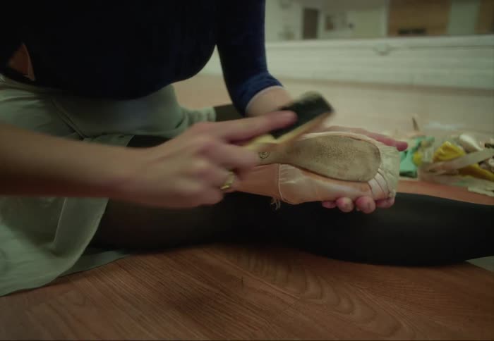 Young ballerina sitting on the floor of a dance studio sanding the soles of her shoes
