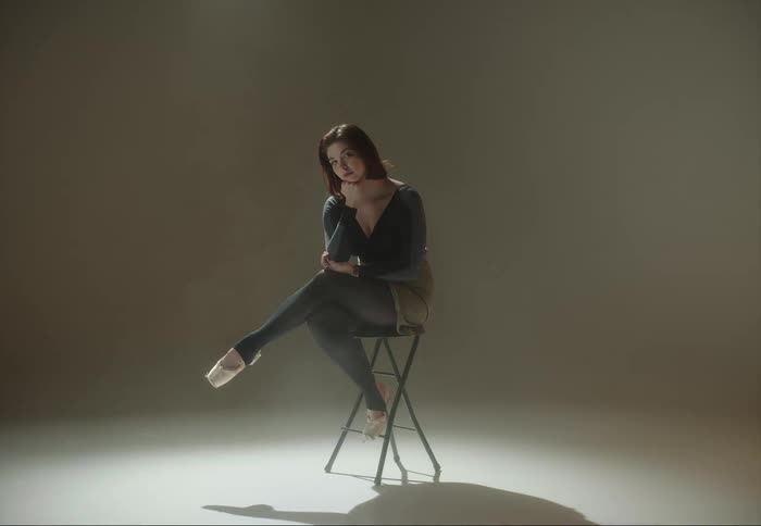 A woman is sitting on a stool and she rests her chin on her hand