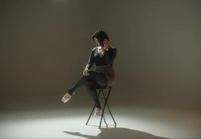 A woman is photographed while sitting on a stool in a photography studio