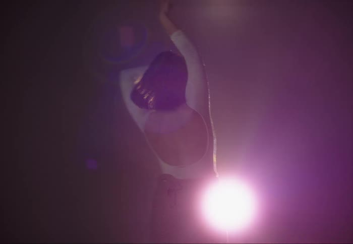 Young female ballet performer dances in front of a colorful spotlight on stage
