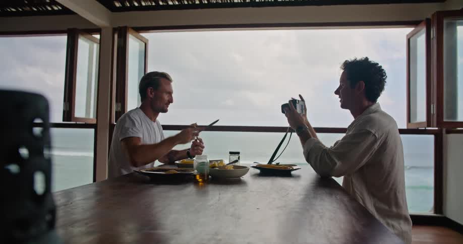 Friends looking at pictures on a camera while eating food on a beachfront apartment