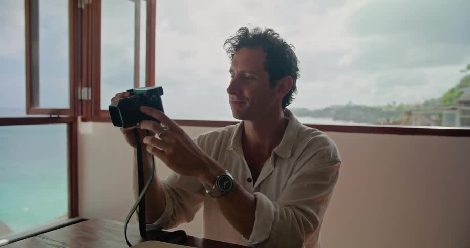 A man eats a forkful of fruit and shows his friend the screen of his digital camera