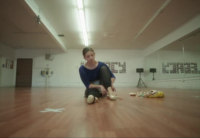 Young ballerina dancer sitting on the floor adjusting her shoes