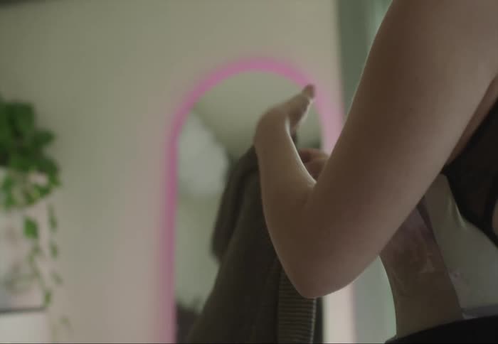 A woman folds a shirt and packs it into a carrying bag while standing in a bedroom