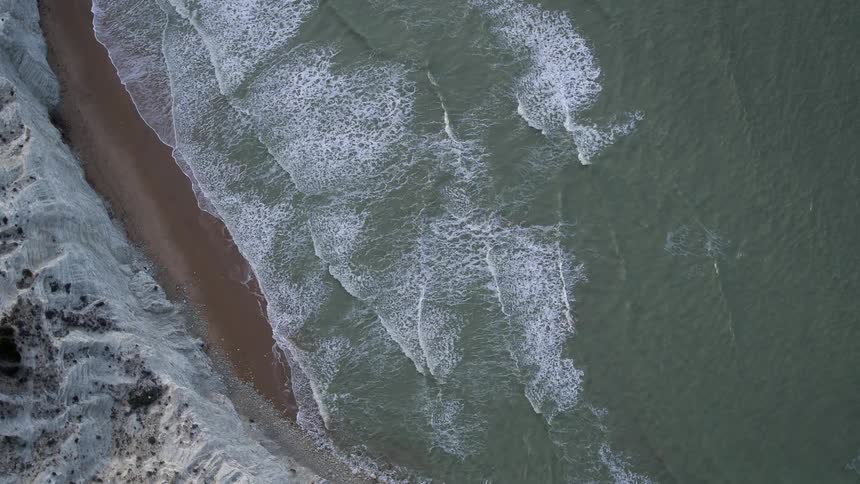 Waves roll in towards the shore beside a rock cliff