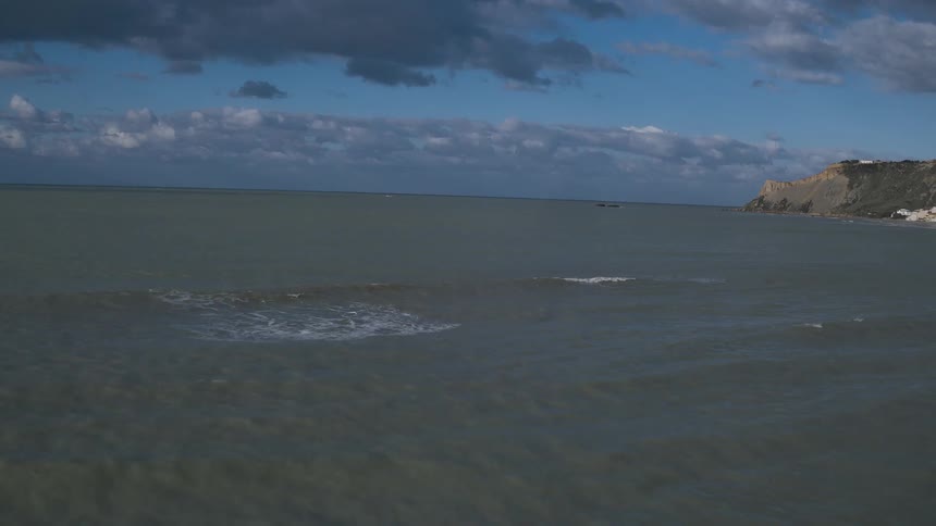 A large expanse of ocean under a blue sky with dark clouds