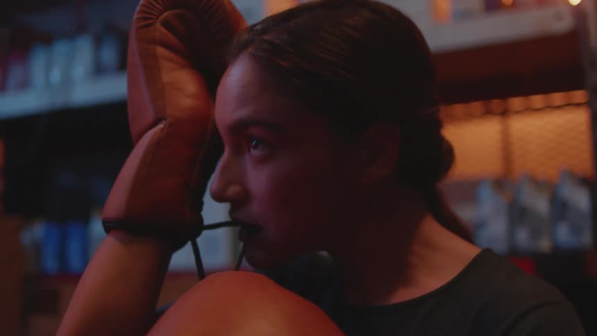 A woman uses her teeth to pull the drawstring on her boxing gloves